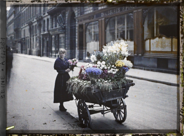 Une marchande de fleurs, en face du 53 rue Cambon, Paris, 1er arr., France, 1918, autochrome , 9×12 cm, Paris, collections du musée Albert-Kahn, inv. A14361 (domaine public, licence CC-00)